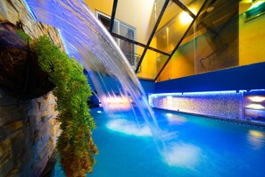 An indoor pool with a waterfall feature, surrounded by stone walls and glass panels. - Little Charm Hanoi Hostel (Hanoi)
