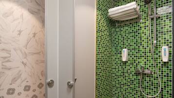 A bathroom with a shower, toilet, and a tiled wall with a green pattern.