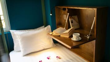 A neatly made bed with white pillows and a wooden bedside table holding a book, a cup, and a lamp.