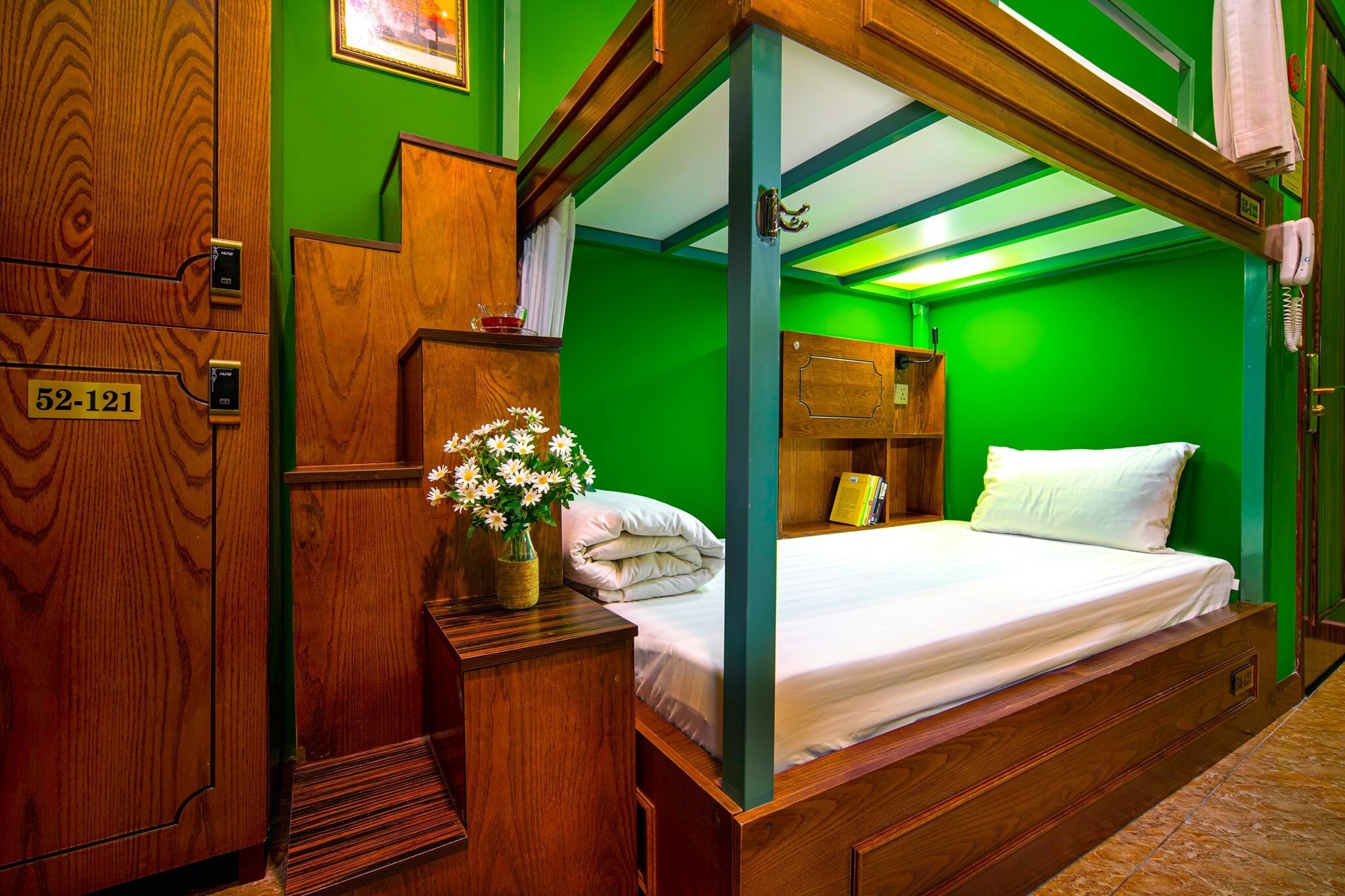 A room with a wooden bunk bed, a bedside table with a vase of flowers, and a green wall.