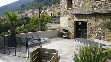 A rooftop terrace with a stone wall, a grill, and a view of a hillside village.