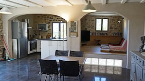 A spacious kitchen with a dining area, stone walls, and a cozy seating area with cushions.