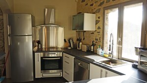 A compact kitchen with a stainless steel refrigerator, oven, and dishwasher. There is a window with a view of the outside, and a stone wall adds a rustic touch to the space.