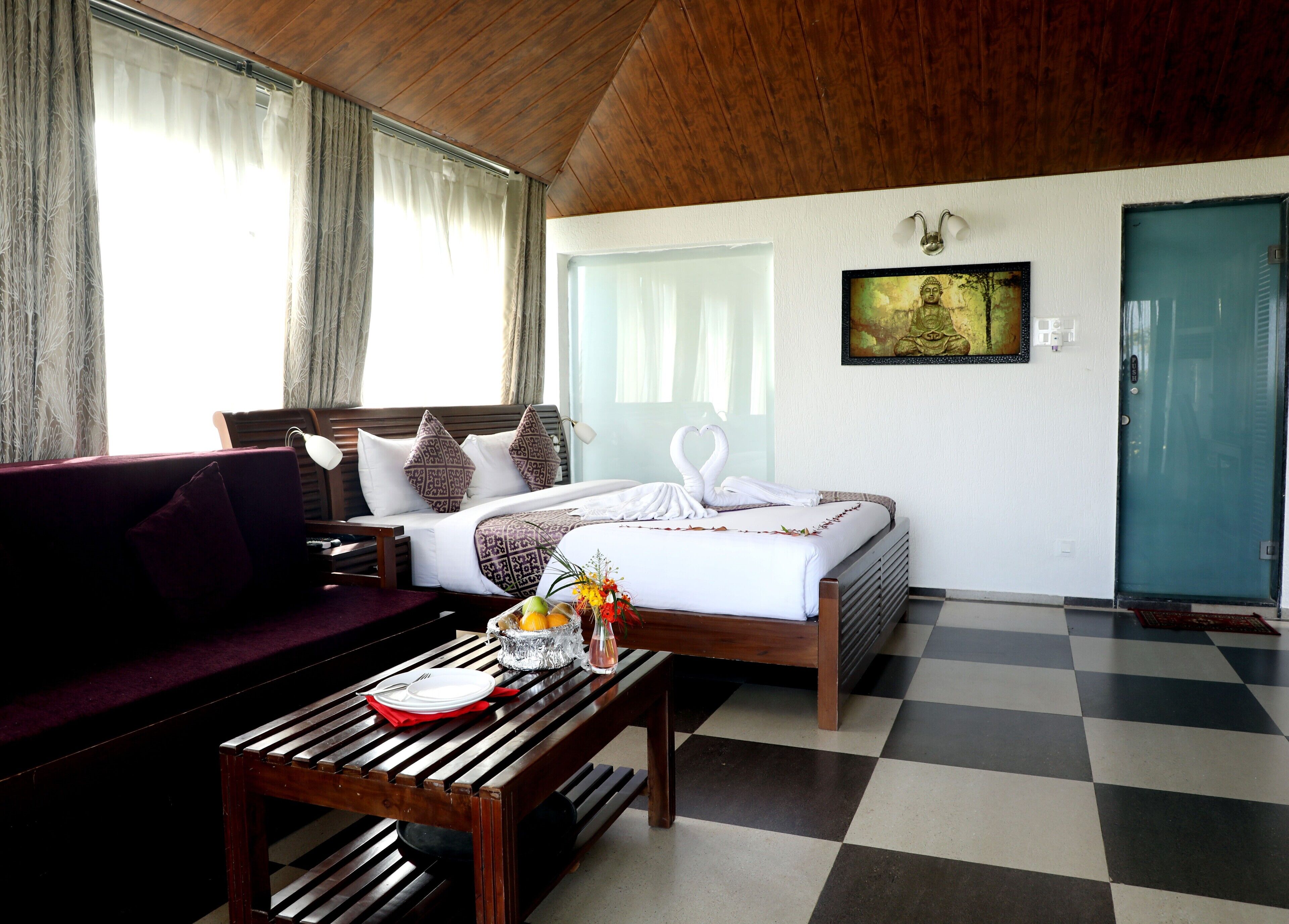 Une chambre d’hôtel avec un lit, un plafond en bois, un sol à carreaux, un canapé, une table avec un panier de fruits et un tableau au mur.