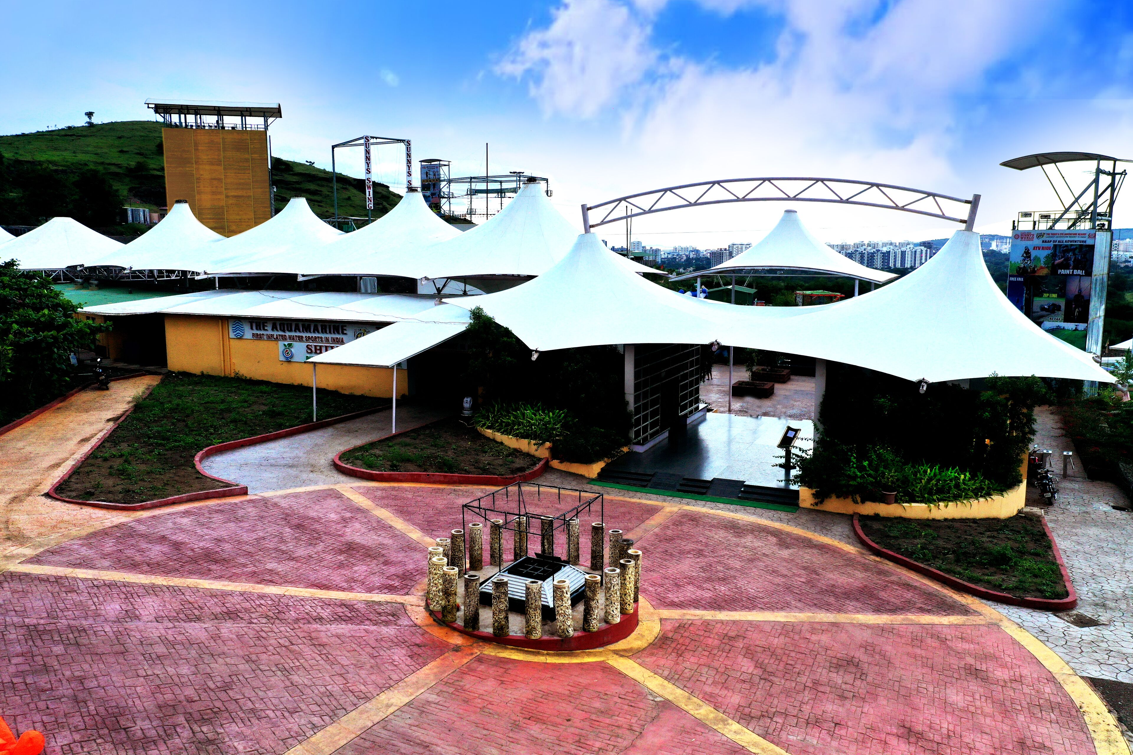 A large, open plaza with a central fountain, surrounded by white canopies and a modern building with a glass facade.