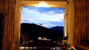A room with a table set for tea, two chairs, and a view of a mountainous landscape. - Sunny's World (Paud)