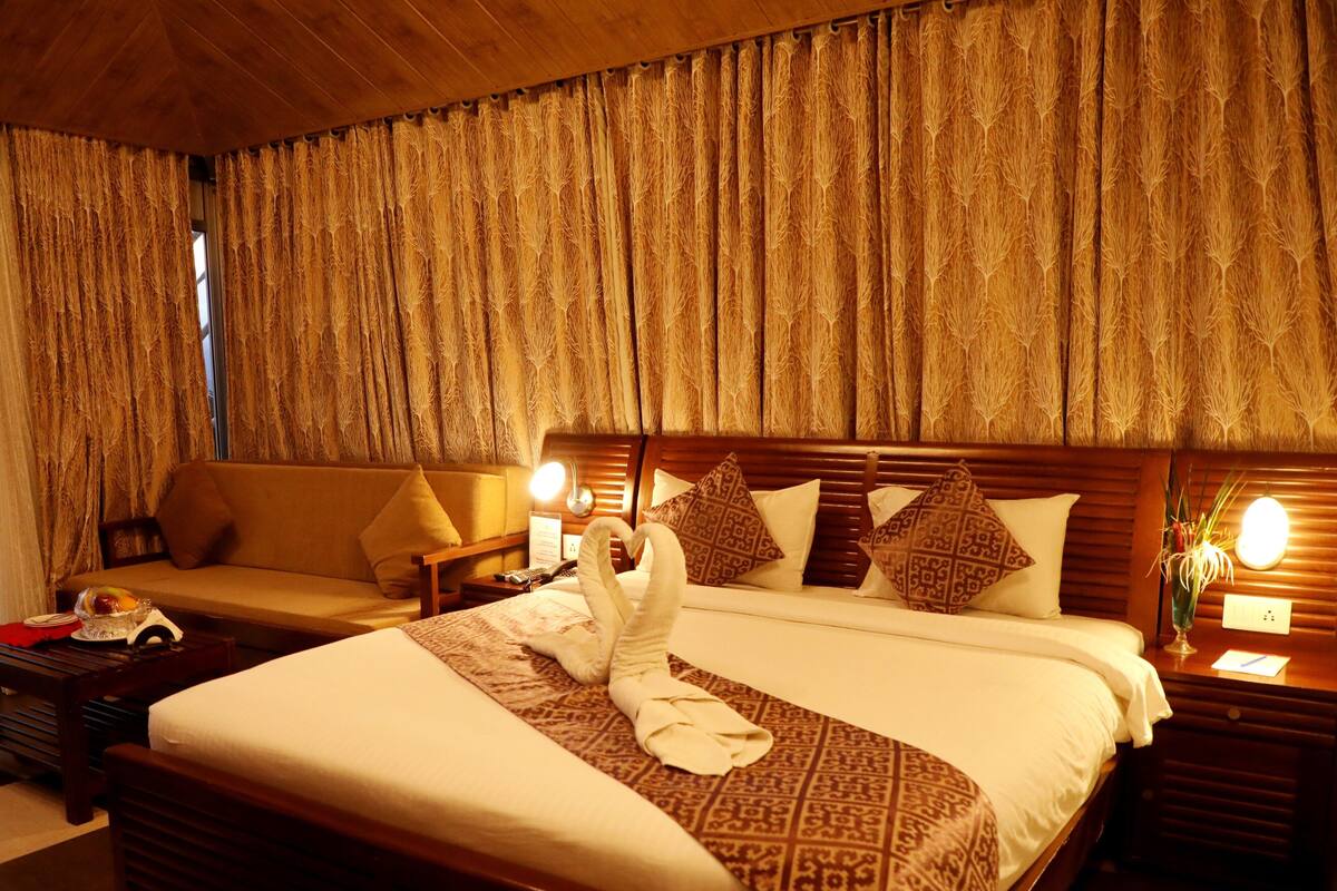 A hotel room with a large bed, a sofa, a bedside table with a lamp, and curtains.