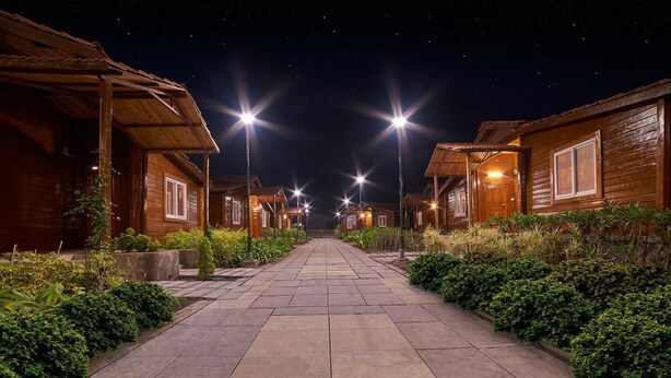 A row of wooden cabins with a paved walkway between them, illuminated by overhead lights. - Sunny's World (Paud)