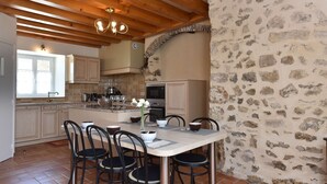 A kitchen with wooden beams, stone walls, and a dining area with chairs and a table.