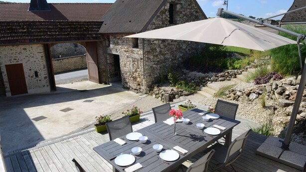 An outdoor dining area with a table set for four, surrounded by stone walls and a wooden deck.