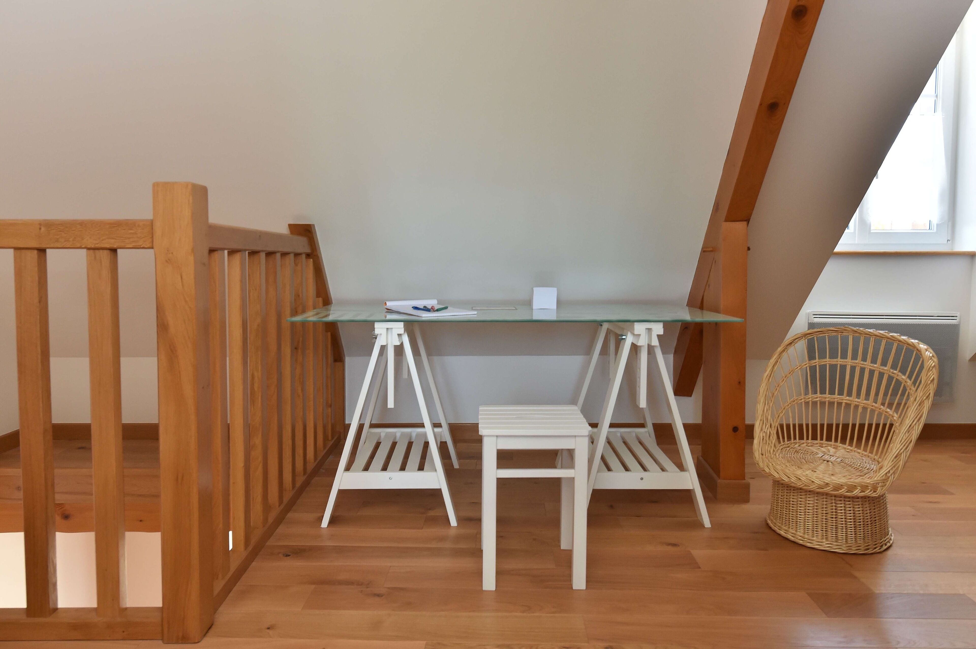 A small, well-lit room with a wooden floor, a glass table, two white chairs, and a wicker chair.