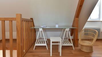 A small, well-lit room with a wooden floor, a glass table, two white chairs, and a wicker chair.
