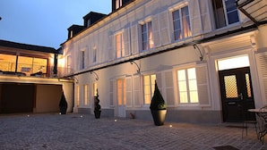 En historisk byggnad med en innergård med kullersten, stora krukväxter och en balkong med utsikt över området.