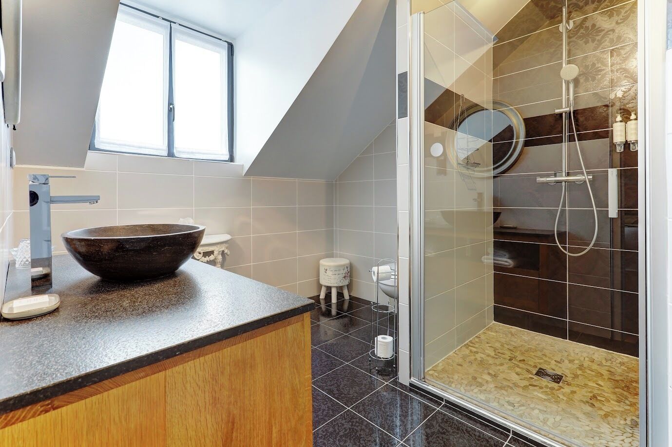 A modern bathroom with a large vessel sink, a glass shower enclosure, and a skylight.