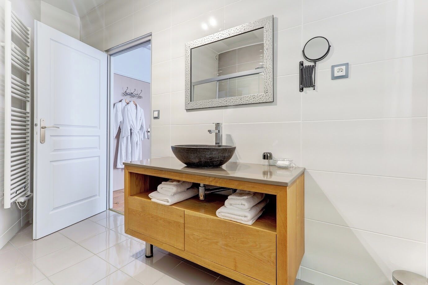 Un baño con tocador de madera, un espejo grande y un espejo redondo, además de un perchero para toallas.
