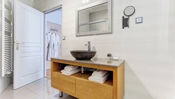 Un baño con tocador de madera, un espejo grande y un espejo redondo, además de un perchero para toallas.