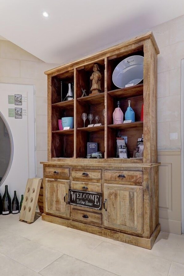 Un mueble de madera con varios estantes, un letrero de bienvenida y diversos objetos, como botellas y una figurita.