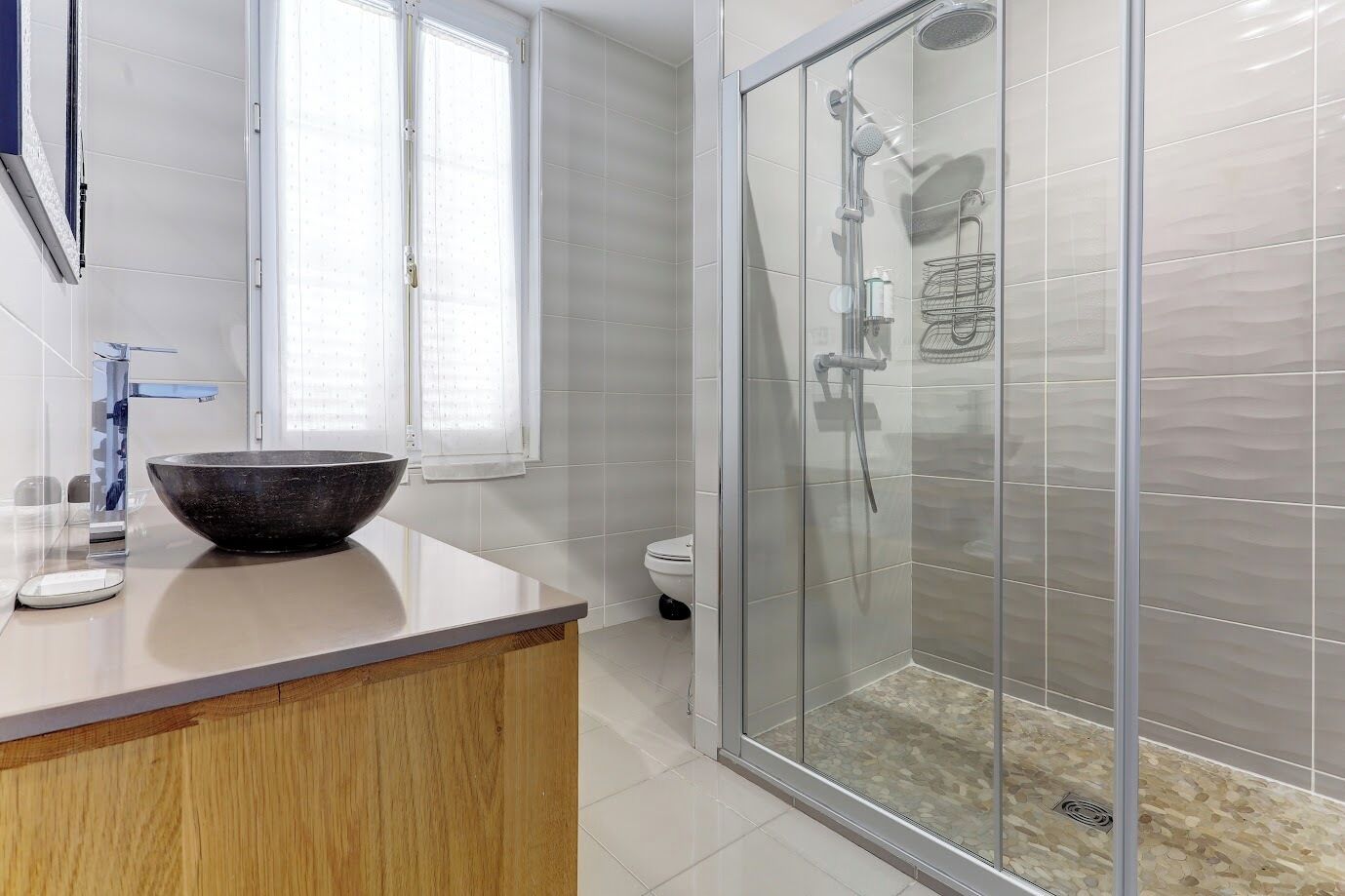 A bathroom with a glass shower enclosure, a large vessel sink, and a toilet.