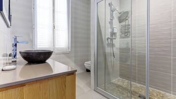 A bathroom with a glass shower enclosure, a large vessel sink, and a toilet.