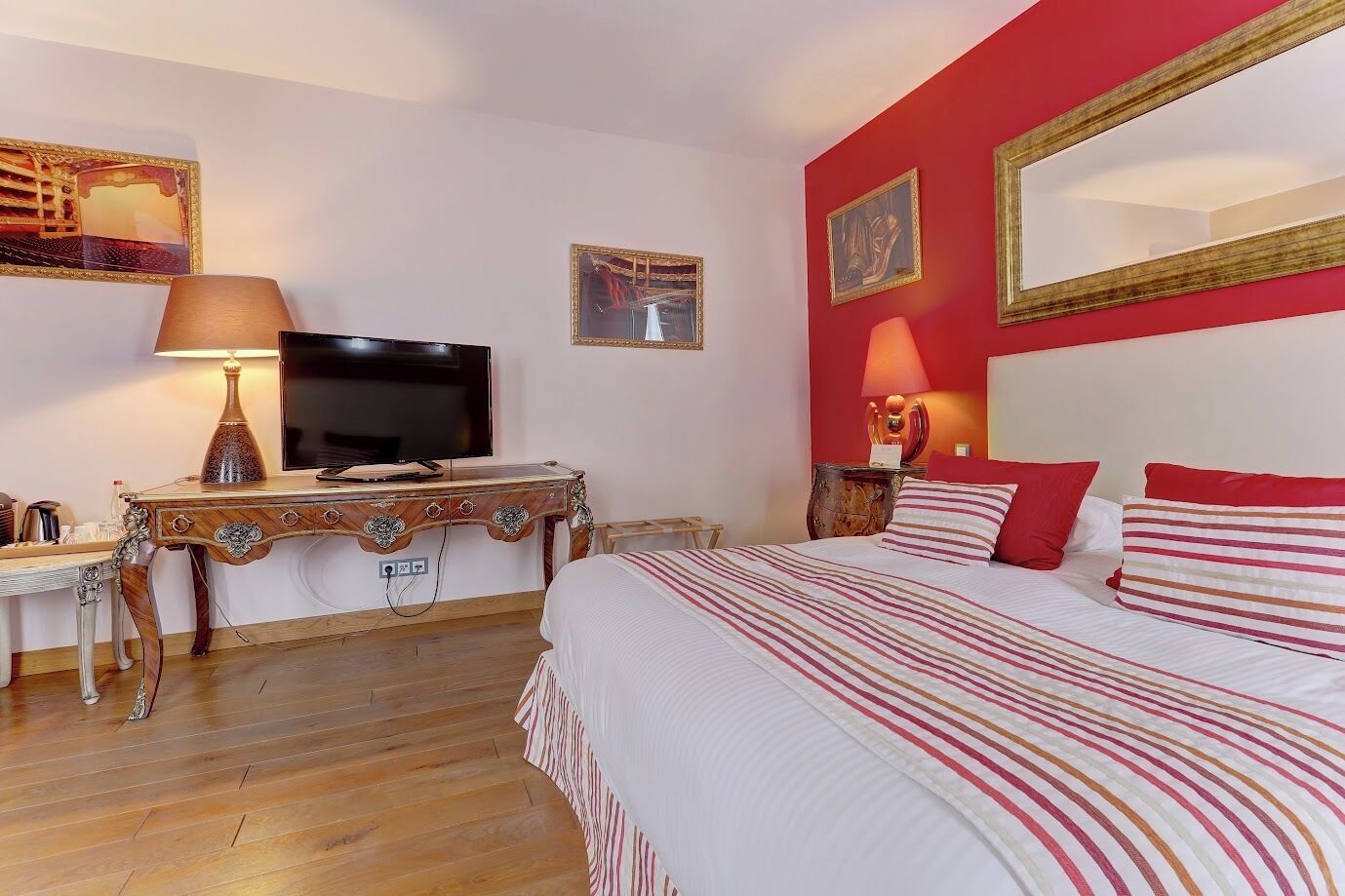 A hotel room with a bed, a desk with a TV, a lamp, and a mirror.