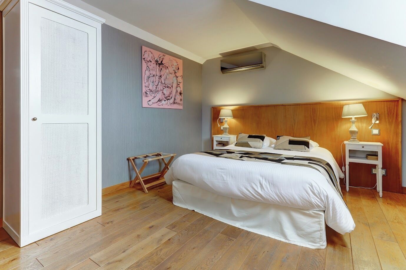Un dormitorio con cama, dos mesitas de noche, un respiradero en la pared, cabecero de madera y una puerta con panel texturizado.