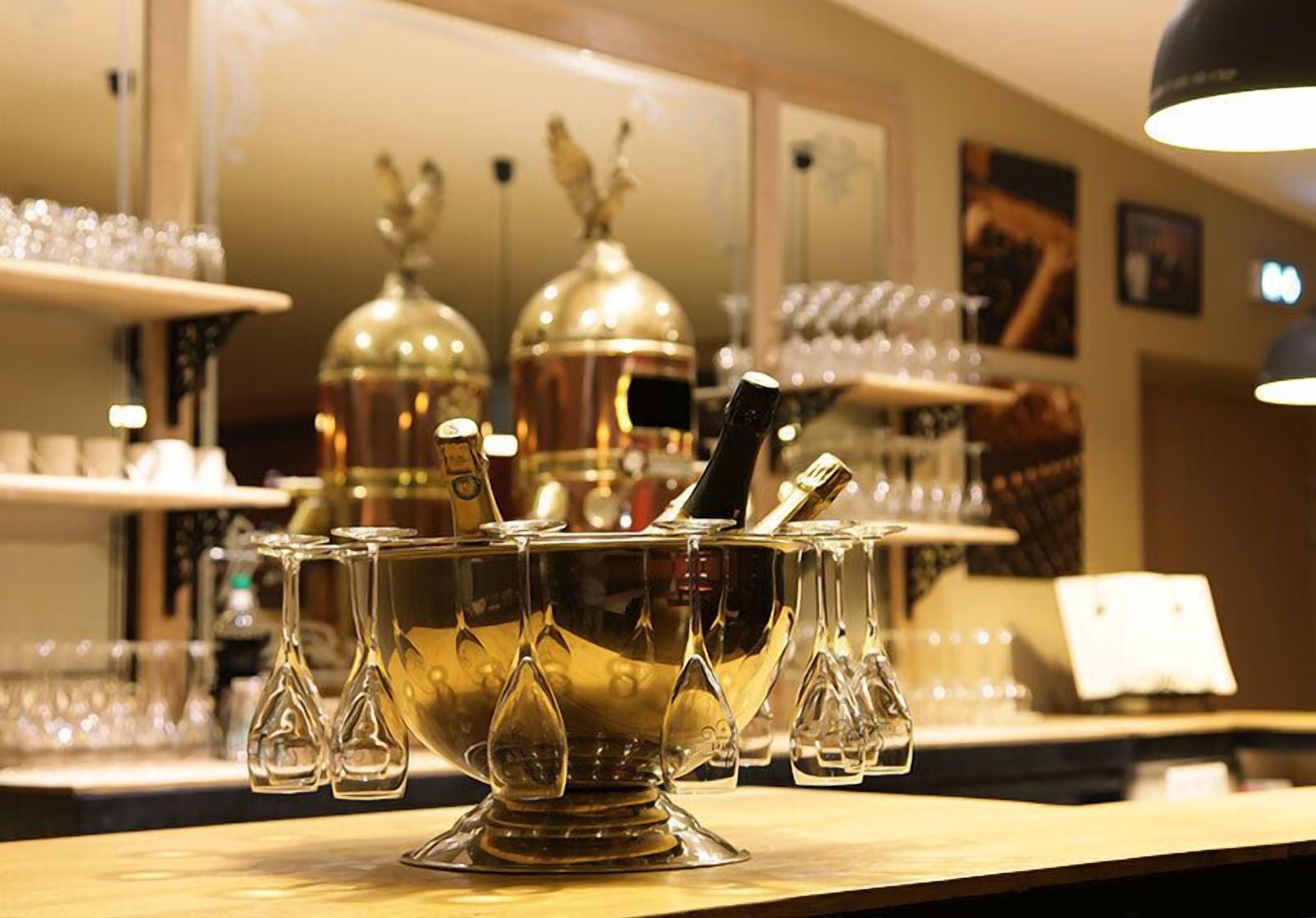 Un espace bar avec un grand et élégant récipient en métal, rempli de verres et d’une bouteille.