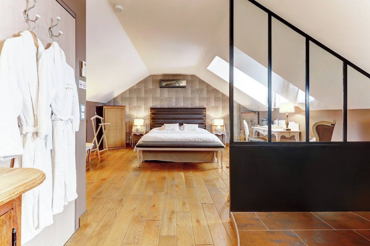A bedroom with a large bed, wooden flooring, a wardrobe, and a view through a window.