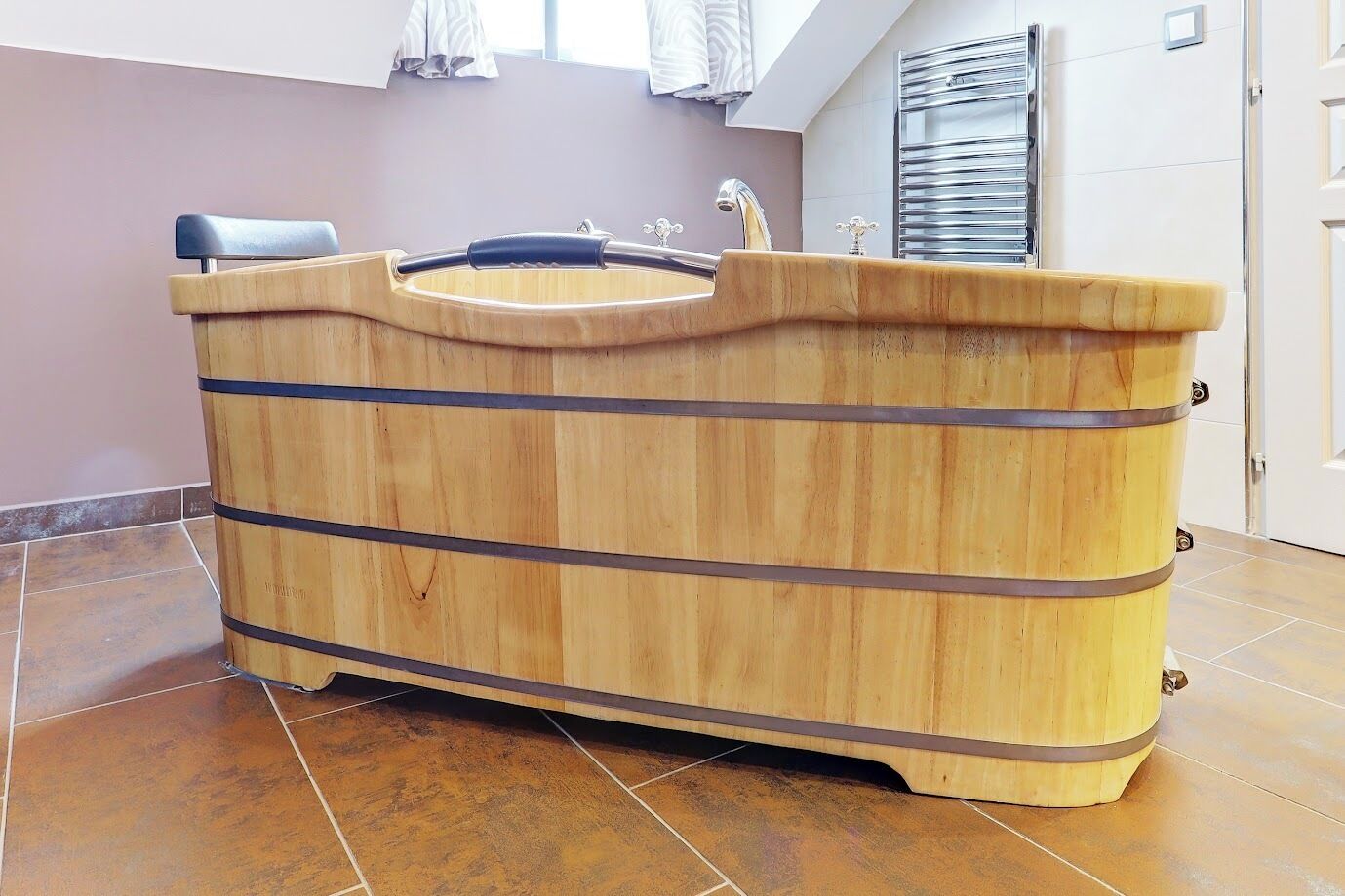 Una bañera de madera con un grifo y un lavamanos pequeño, ubicada en una habitación con suelo de baldosas y una puerta al fondo.