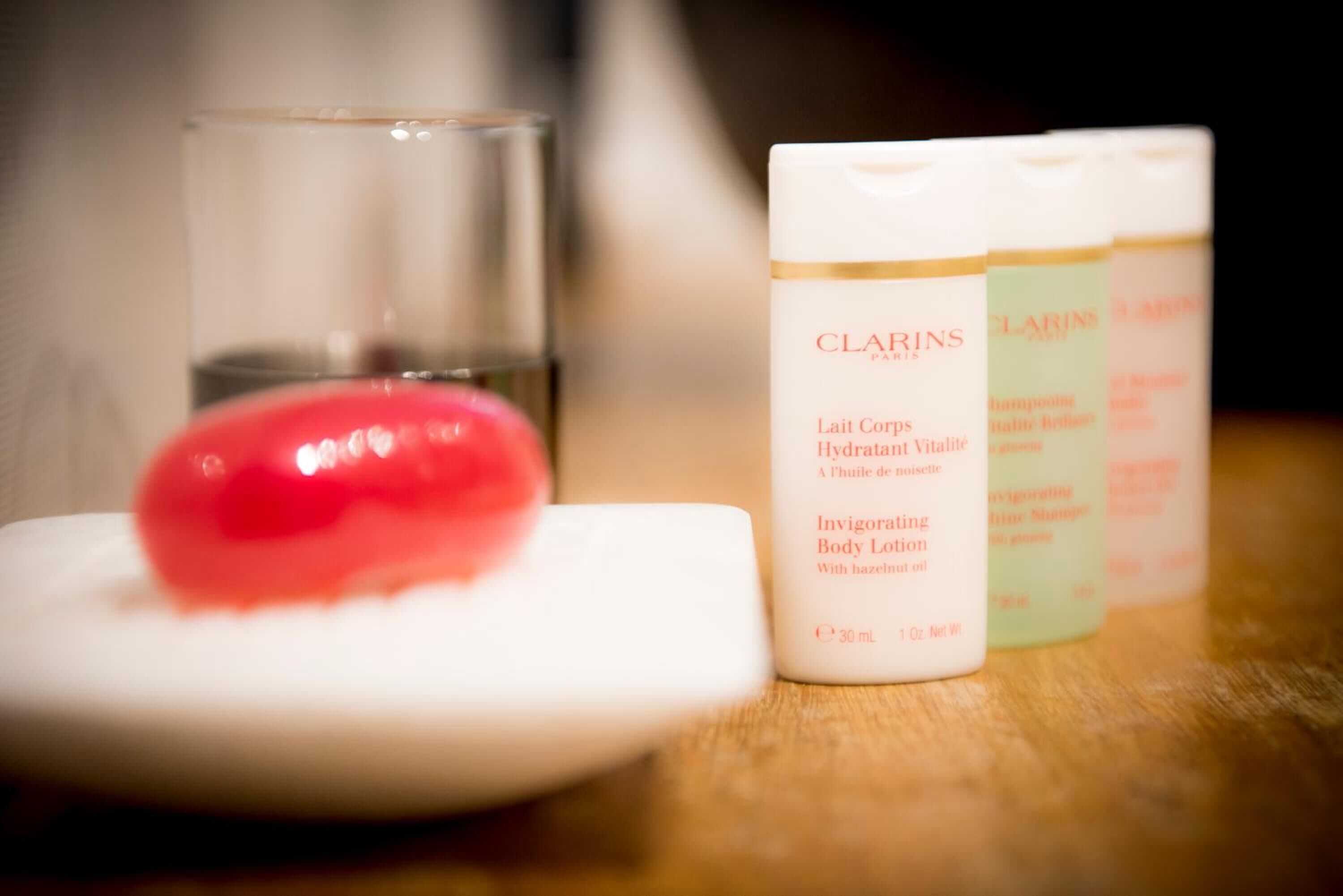 Un plato blanco con un objeto rojo, posiblemente mermelada, y tres botellas de loción corporal Clarins.