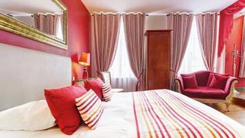 Quarto de hotel com uma cama grande, uma poltrona vermelha, um guarda-roupa de madeira e um espelho na parede.