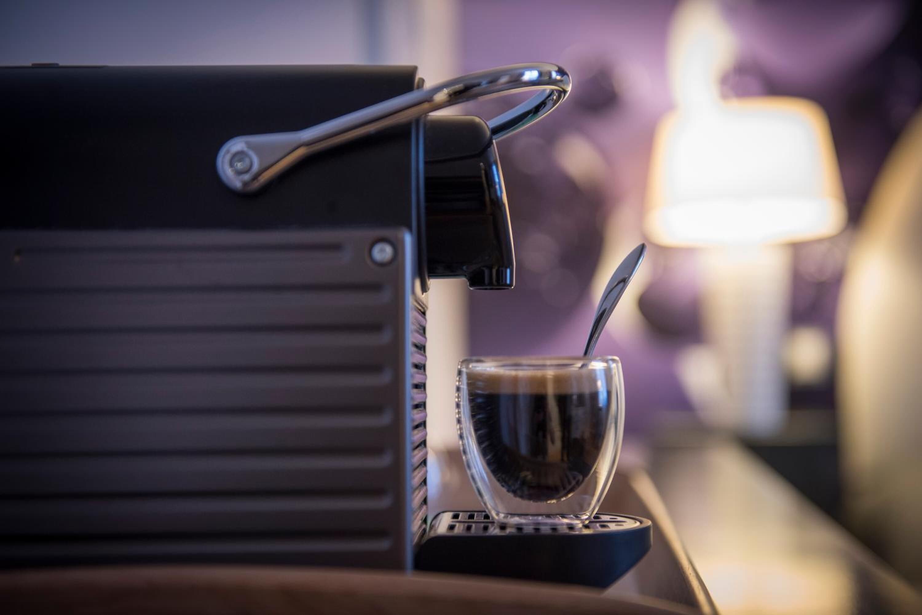 A coffee machine with a cup and spoon on a tray.