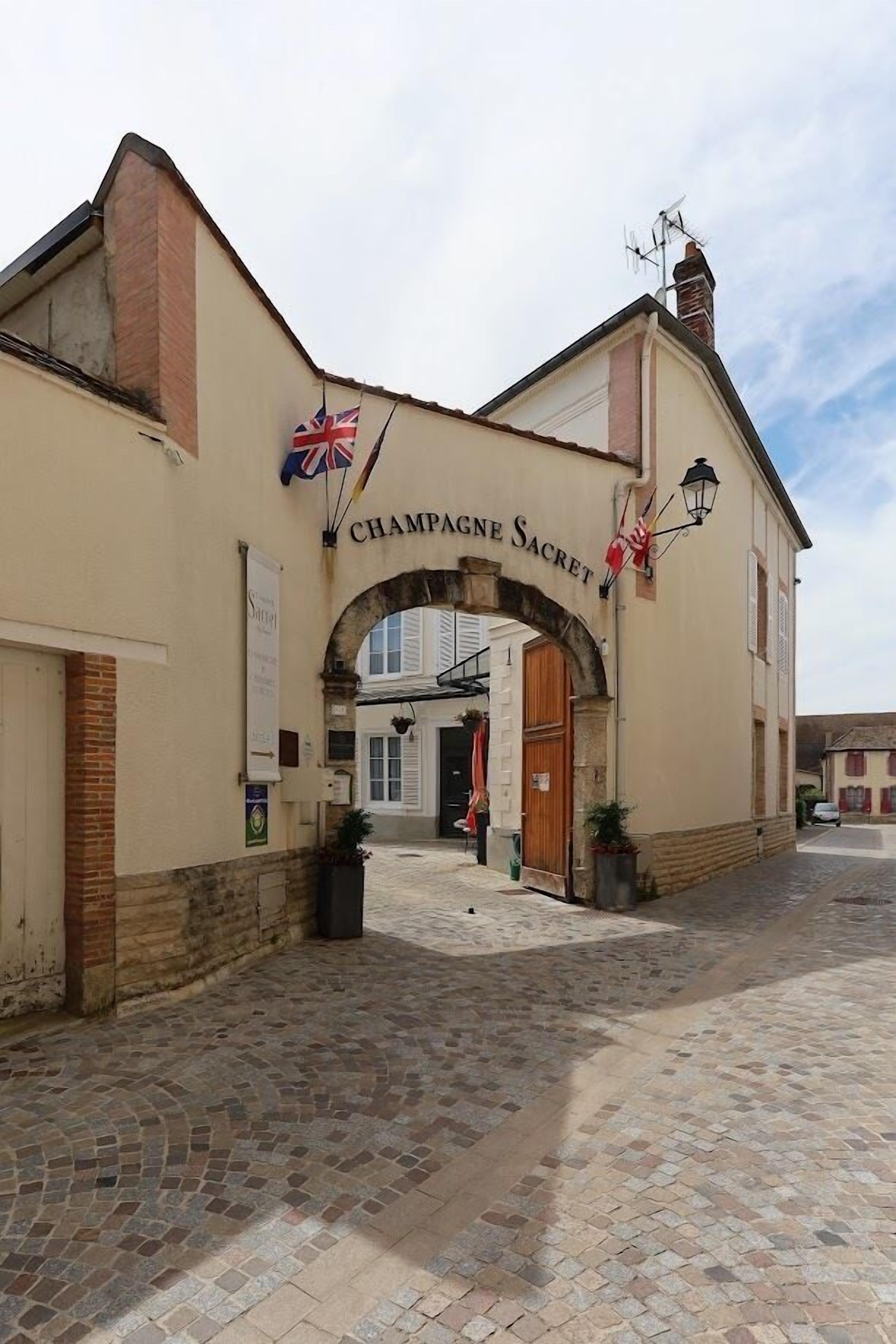 Un bâtiment doté d’une arche sur laquelle on peut lire « Champagne Sacret » et sur lequel flotte un drapeau britannique.