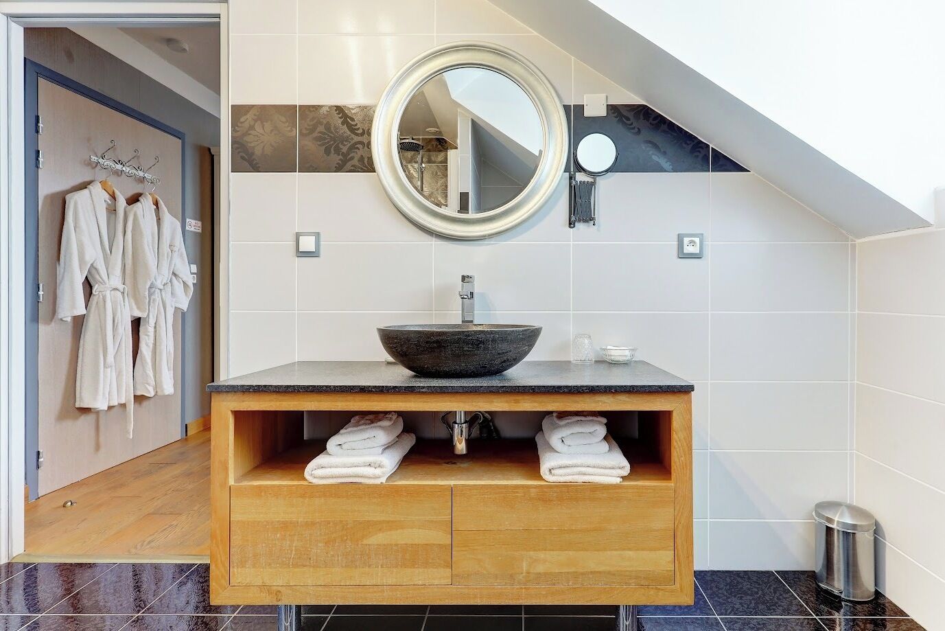 Une salle de bain moderne avec un meuble-lavabo en bois, un grand miroir rond et un lavabo sur colonne.