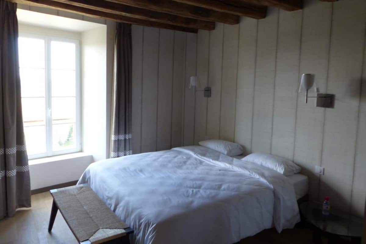 A bedroom with a bed, a bench, a nightstand, and a window with curtains.