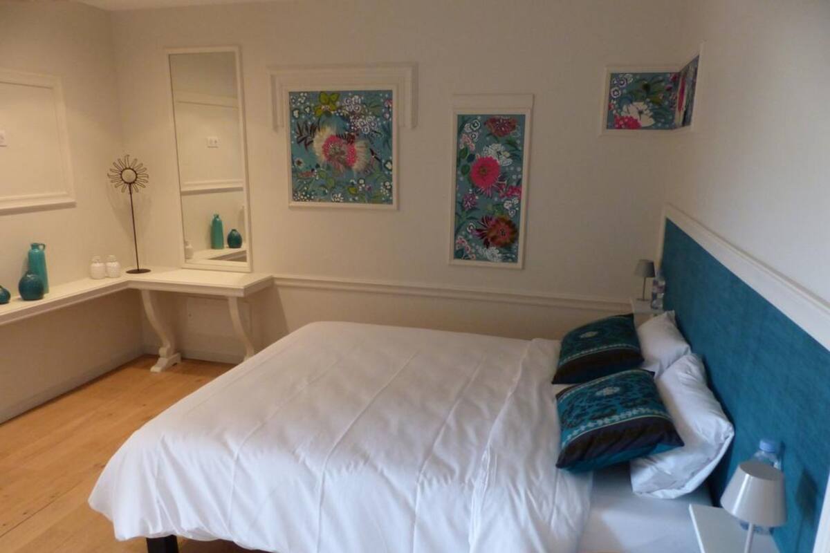 A bedroom with a large bed, a bedside table with a lamp, and floral artwork on the walls.