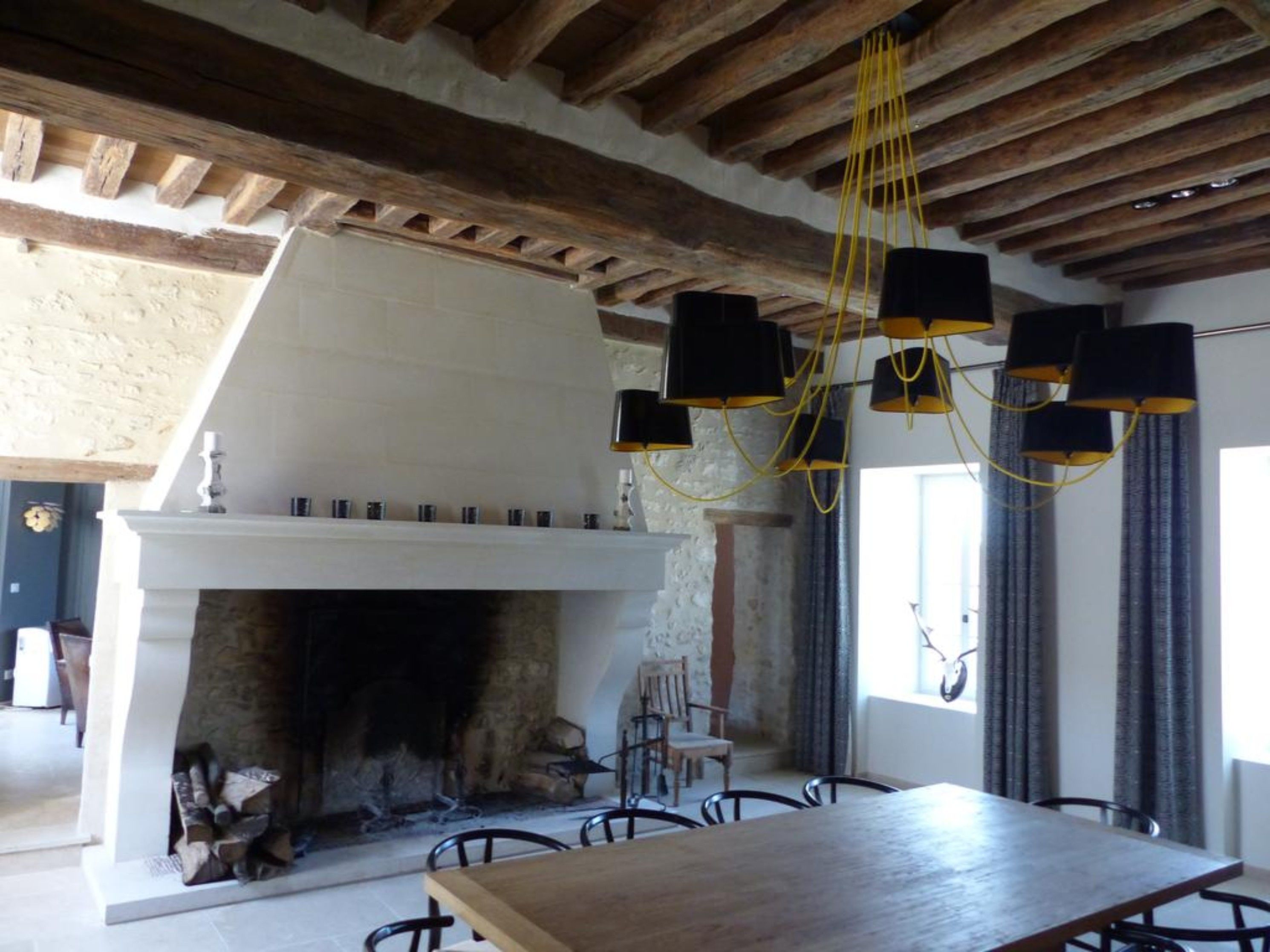 A dining area with a fireplace, wooden beams, and a chandelier.
