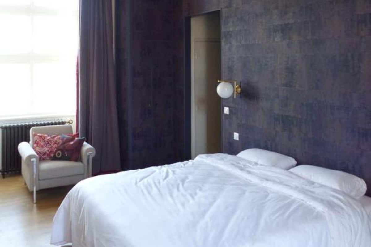 A bedroom with a large bed, a chair, a window with curtains, and a wooden ceiling.