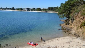 A beach with clear water, a red kayak, and a person walking.