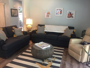 Relax in this stylish living space with a sofa, ottoman, and armchair, surrounded by artwork and a view of lush greenery.