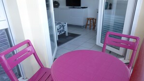 A balcony with a pink table and chairs, a kitchen area in the background, and a sliding glass door.