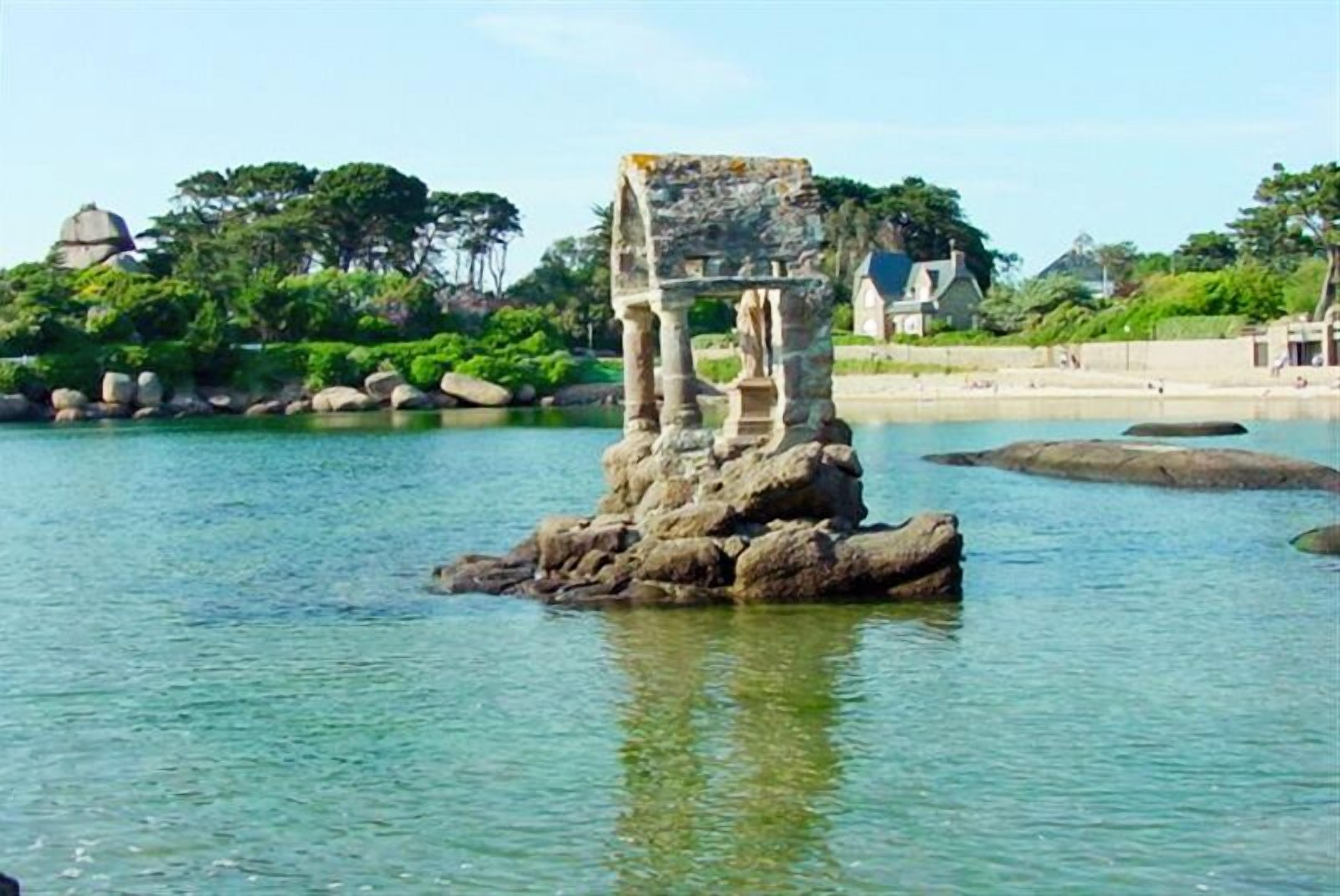 A rock formation with a structure on top, surrounded by water and greenery.