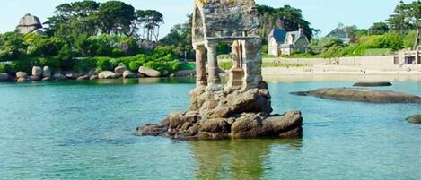 A rock formation with a structure on top, surrounded by water and greenery.