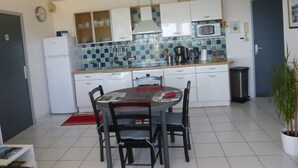 A compact kitchen with white cabinets, a microwave, and a tiled backsplash. There is a dining table with chairs and a red rug on the floor.