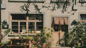 A building with multiple windows, some with curtains, and a wooden table with potted plants in front. - Loku.Tainan (Tainan)
