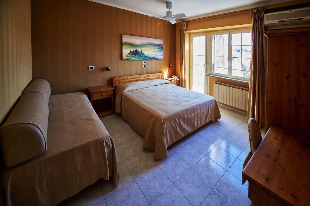 A room with two beds, a wooden headboard, a painting on the wall, a window with curtains, and a wooden table.