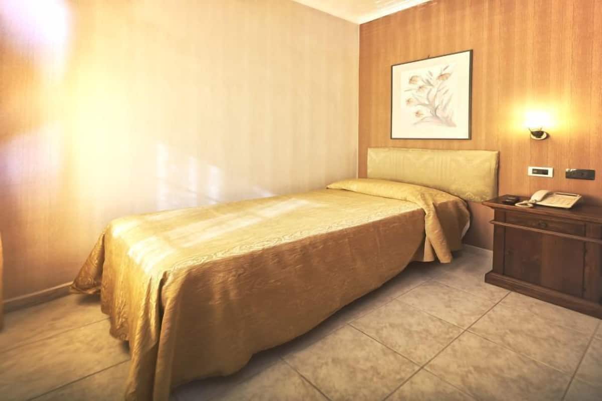A single bed with a headboard, a bedside table with a lamp, and a framed picture on the wall.