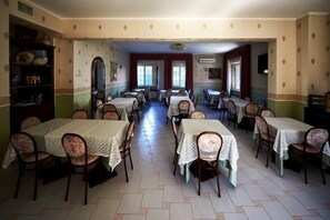 A dining area with multiple tables and chairs, a bookshelf, and a television. - Hotel La Brocca (Fonte Nuova)