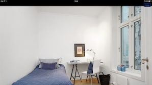 A small, well-lit room with a bed, a desk, and a chair. There is a window with a view of buildings outside. - Apt. Odins Gate (Oslo)