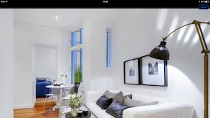 A modern living room with a white sofa, a coffee table, and a floor lamp. There is a dining area with a table and chairs in the background. - Apt. Odins Gate (Oslo)