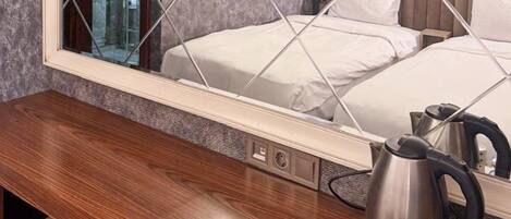 A hotel room with a large mirror, two beds, a wooden desk, a kettle, and a coffee maker.